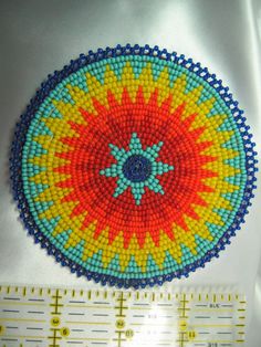 a close up of a piece of beaded art with a ruler in the foreground