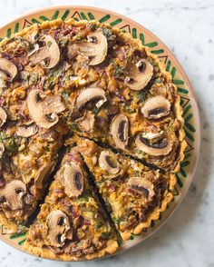 a pizza with mushrooms on it sitting on top of a green and yellow plate next to a knife