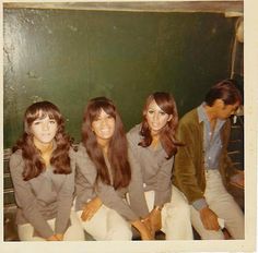 three young women sitting on the back of a white couch in front of a green wall