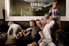 a family sitting on a couch in front of a large painting with a house behind them