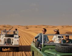 four people are riding in the back of a green jeep and two men are driving behind them