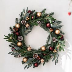 a christmas wreath hanging on the wall with pine cones and evergreen leaves, ornaments and berries