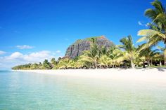 the beach is lined with palm trees and mountains in the distance, as well as clear blue water