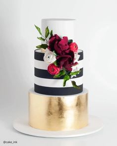 a white and black striped cake with red flowers on the top, gold plated platter