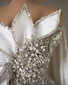 the back of a white dress with silver sequins on it and a large flower in the center