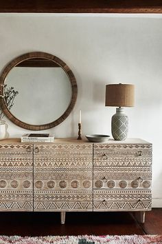 a white dresser sitting next to a mirror on top of a wooden floor covered in rugs