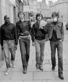 four young men walking down the sidewalk with one holding a coffee cup