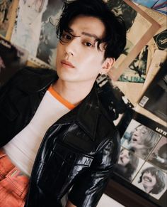 a young man with black hair and glasses posing in front of a wall full of posters