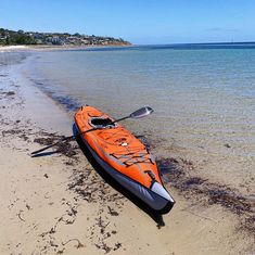 an orange kayak sitting on top of a sandy beach