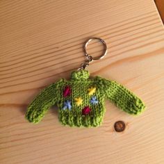 a green knitted sweater keychain sitting on top of a wooden table next to a button