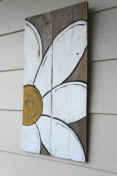 a painted wooden sign on the side of a house with white and brown flowers hanging from it's sides