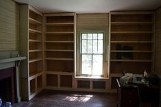 an empty room with wooden shelves and a fireplace in the corner, next to a window