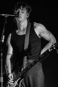 black and white photograph of a man playing an electric guitar on stage with microphone in front of him