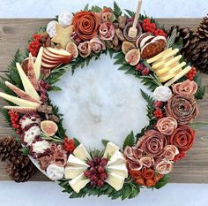 a christmas wreath made out of apples, pine cones and other holiday decorations on a wooden surface