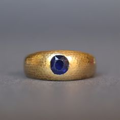 A beautiful vintage sapphire band dating to the Art Deco era (1920-1945). The vibrant blue of the cushion cut sapphire  is perfectly complemented by the textured finish of the 14ct yellow gold setting. The interior of the band has a personalised engraving reading '1911 1931'. An understated piece with a domed profile and clean lines, this ring is perfect for stacking or for wear on its own. Stamped '585' for 14ct gold. Size P ½ (US 8.25). Can be resized within reason. Weight (approximate): 7.8g Measurements (approximate): The band measures 8mm at the widest point, tapering to 3.5mm. The sapphire measures 5.25mm x 4.75mm (estimated to be 0.5 carat weight). Condition: Good, with wear commensurate with age. The table facets of the sapphire have some abrasion. The band shows evidence of resizi Art Deco Gold Ring, Saphir Ring, Vintage Sapphire, Sapphire Band, Yellow Gold Setting, Art Deco Era, Vibrant Blue, Stackable Rings, Cushion Cut