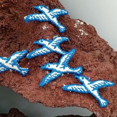 three blue and white embroidered airplanes on a brown rock next to another piece of red clay