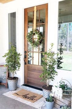 two potted plants sit on the front porch next to a door with a welcome mat