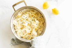 a pot filled with pasta and cheese on top of a white counter next to two lemons