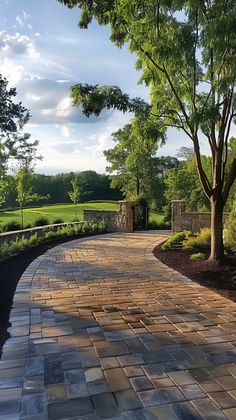 a brick walkway with trees and bushes on either side in front of a grassy field