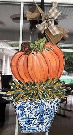 a decorative pumpkin sitting on top of a blue and white hexagonal vase with a bow