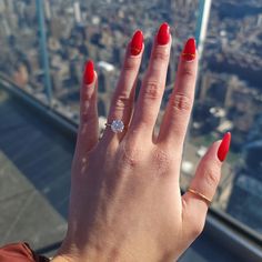 a woman's hand with red nails and a ring on top of a building