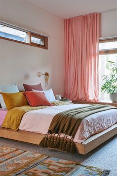 a bedroom with a bed, rugs and pink drapes on the windowsill