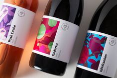 three bottles of wine sitting next to each other on a white counter top with colorful designs