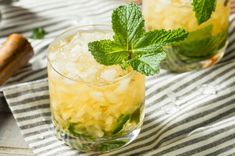 two glasses filled with ice and mint on top of a striped cloth next to a shovel