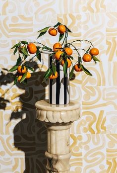 there is a vase with oranges in it on the table next to a wall