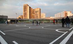 several people are playing basketball in an empty parking lot with buildings in the background at sunset