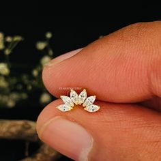 a hand holding a small diamond ring in it's left hand, with white flowers in the background