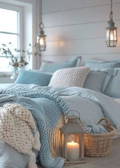 a bed with blue comforters and blankets on it, next to a candle in a wicker basket