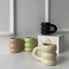 three ceramic mugs sitting next to each other on a white counter with a box