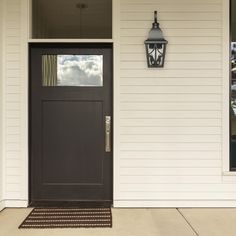 a black front door on the side of a white house with a light hanging above it