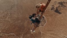 two people standing on top of a metal structure in the desert, looking down at something