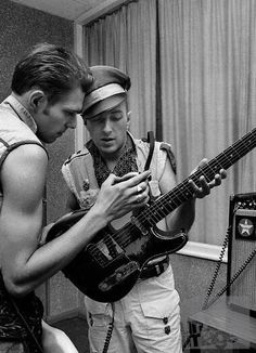 two young men are looking at their cell phones while they play music on the guitar