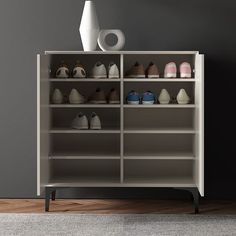 a shelf with shoes and vases on top of it in front of a gray wall