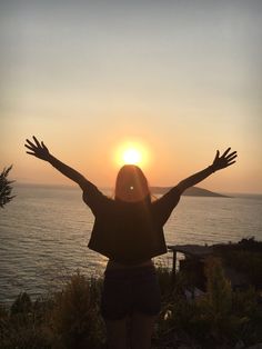 a woman standing on top of a hill with her arms outstretched in front of the sun