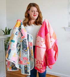 a woman holding two colorful quilts in her hands