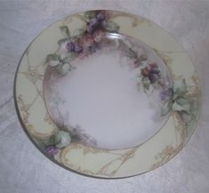 a plate with flowers painted on it sitting on a white tablecloth covered table cloth