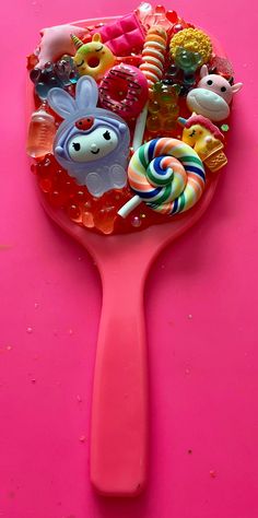 a pink spoon filled with candies and lollipops on top of a pink surface