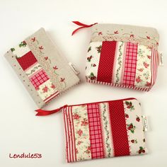 three small purses with red and white designs on them, one in the shape of a cross