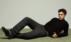 a young man laying on the ground with his legs crossed, wearing a black sweater and jeans