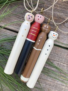 three wooden toy figures hanging from a string on a wood surface with pine needles and branches