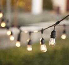 some light bulbs are hanging from a string on the grass in front of a building