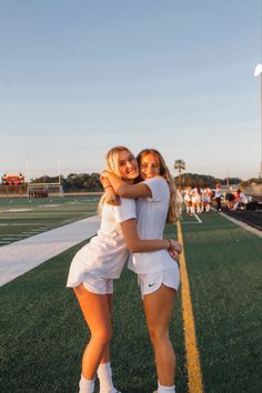 two girls hugging each other on the sidelines of a soccer field with people in the background