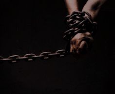 two hands holding chains in the dark, with one hand wrapped around the other's wrists