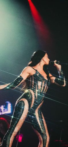 a woman in black and white outfit on stage with lights behind her holding a microphone