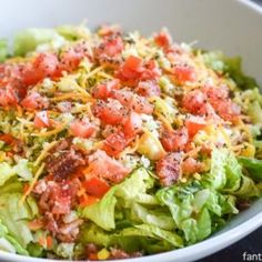 a white bowl filled with lettuce, tomatoes and other toppings on top of it