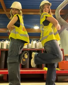 two women in yellow vests and hard hats standing next to each other with construction equipment behind them